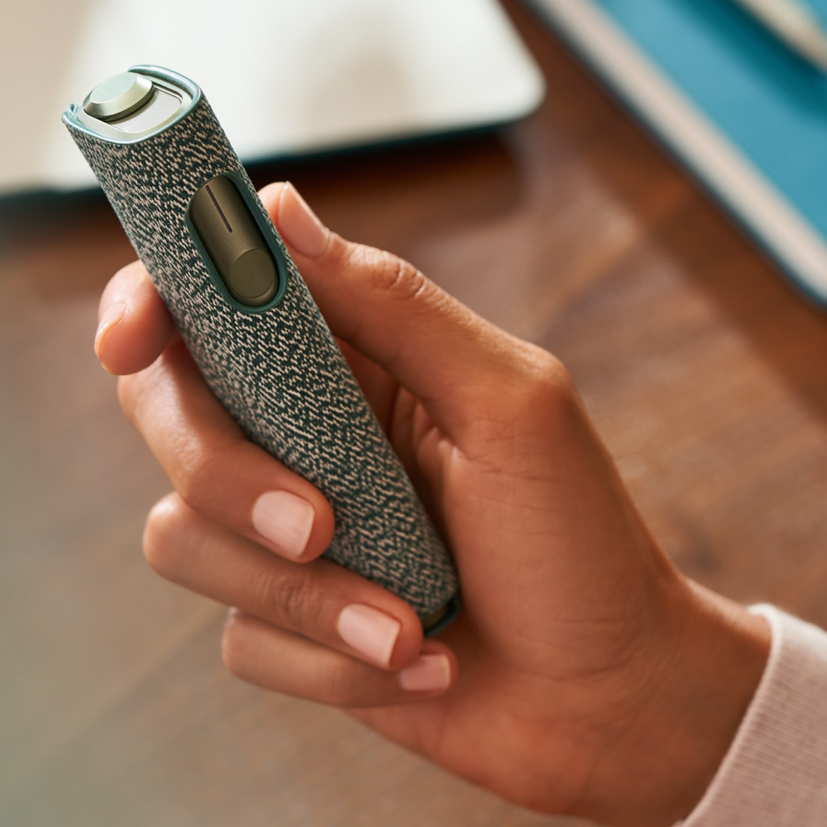 Hand hält IQOS ILUMA ONE in Pepple Beige mit Hülle